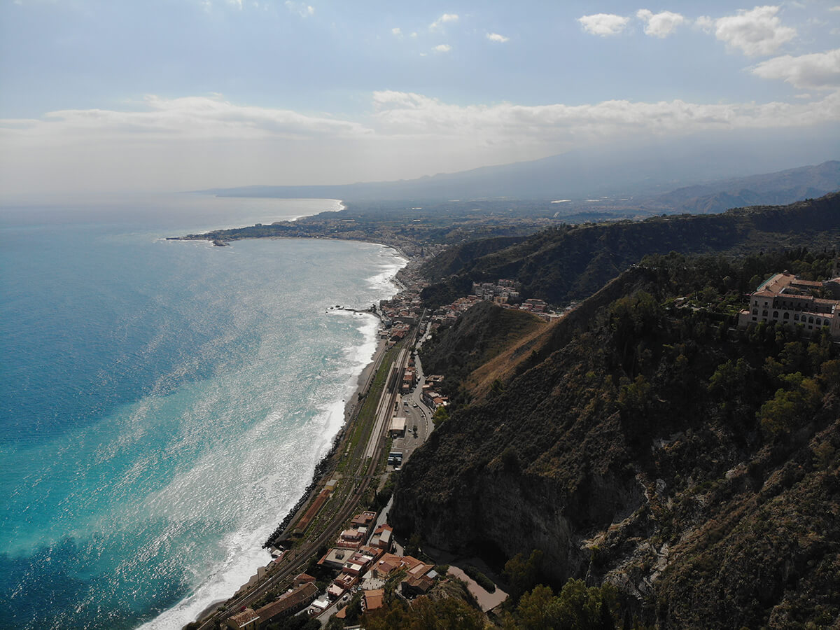 drone shot above taormina mountain and the ocean 