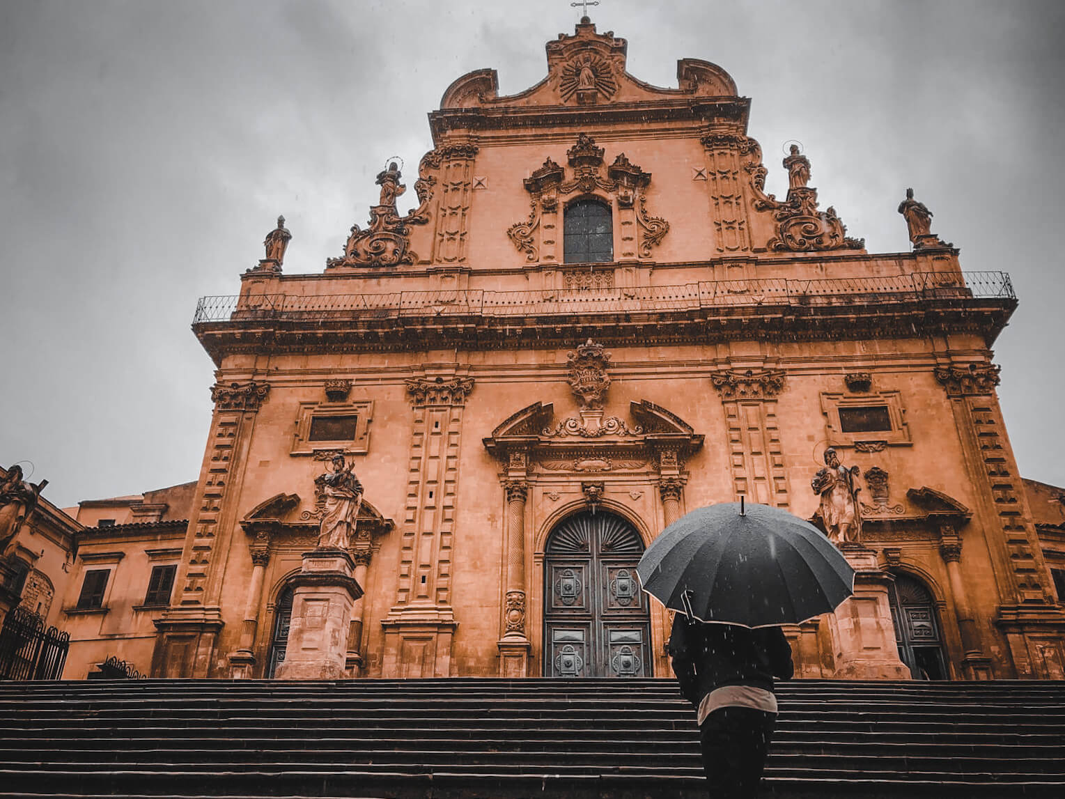 guy standing with umbrella in the rain and looking at modica Cathedral in sicily
