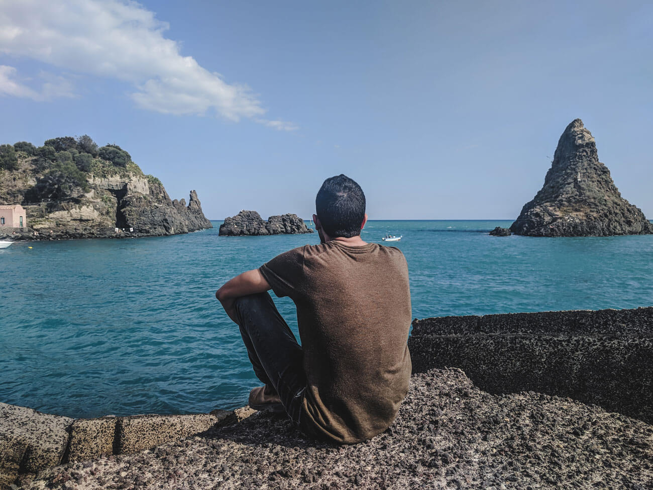 a guy looking at big rocks on the water Cyclops island in sicily