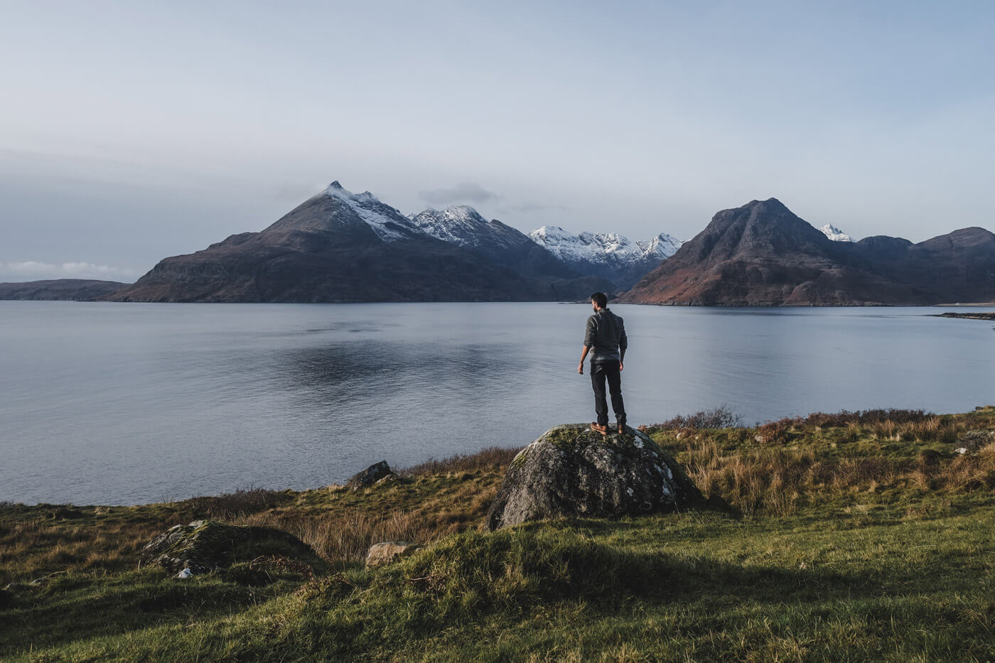 man standing on a rock with ocean and Mountains view in isle of skye